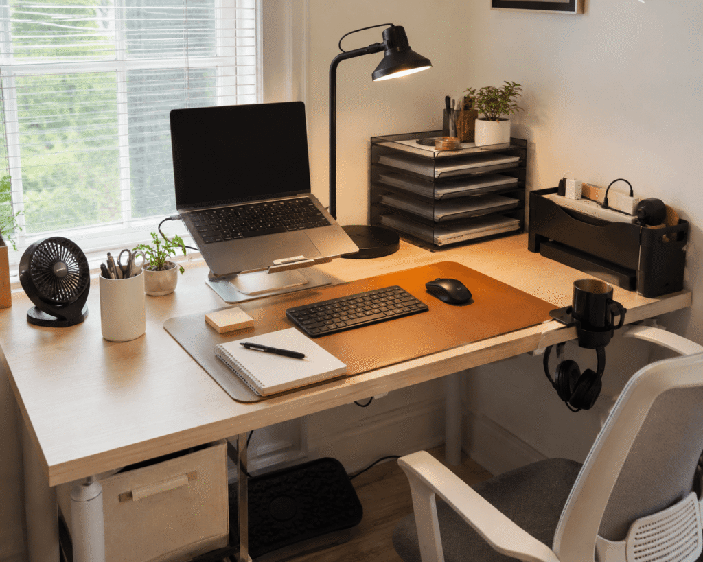 Small home office setup with affordable desk accessories under $30, including a laptop stand, desk mat, lamp, organizer and desk fan.